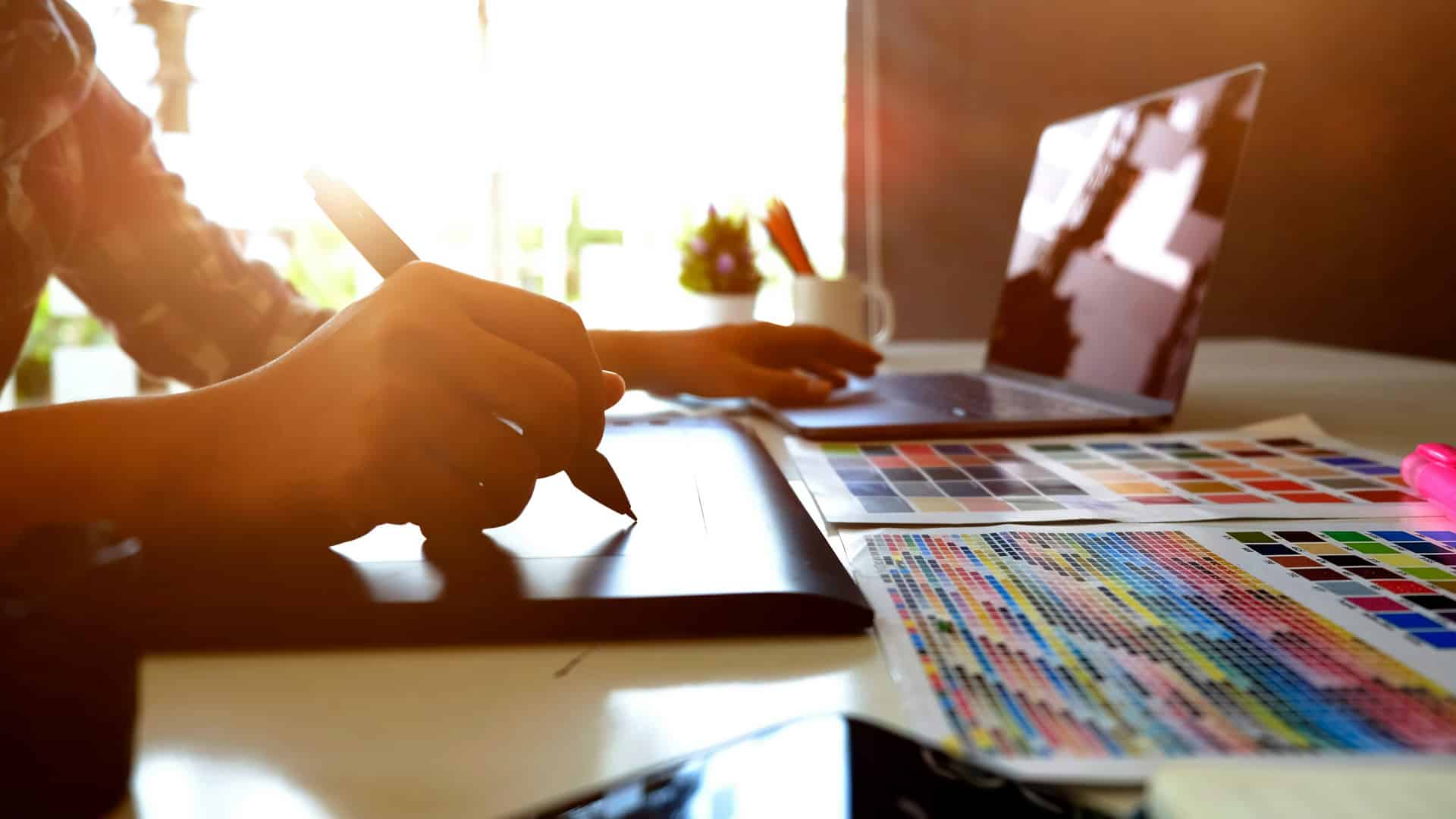 Designer working on a digital tablet and laptop with color palettes in the foreground, symbolizing creative visual branding and website design